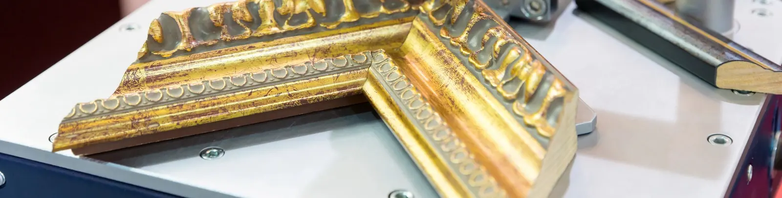 Ornate gold moulding held in a mitre clamp on the joining bench